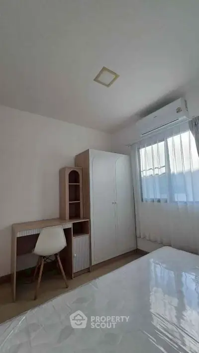 Cozy bedroom with modern furniture and natural light, featuring a desk and wardrobe.