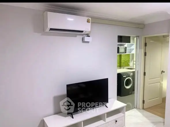 Modern living room with air conditioning and TV, view into laundry area with washing machine.