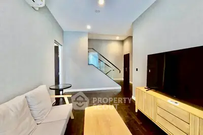 Modern living room with sleek furniture and TV, featuring a stylish staircase and elegant lighting.