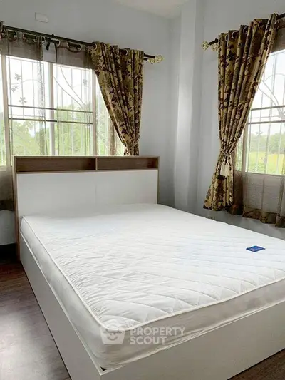 Cozy bedroom with large windows and elegant curtains, featuring a comfortable bed and serene natural light.