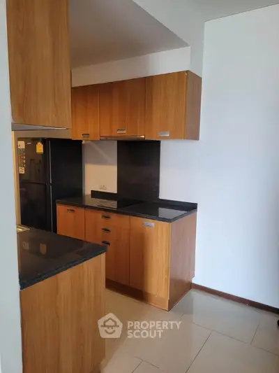 Modern kitchen with wooden cabinets and sleek black countertops in a contemporary apartment.
