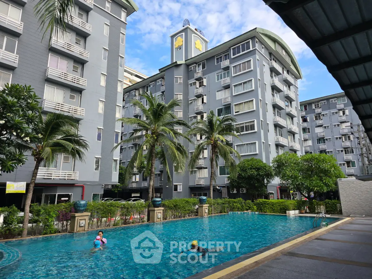 Modern apartment complex with swimming pool and palm trees under a clear blue sky.