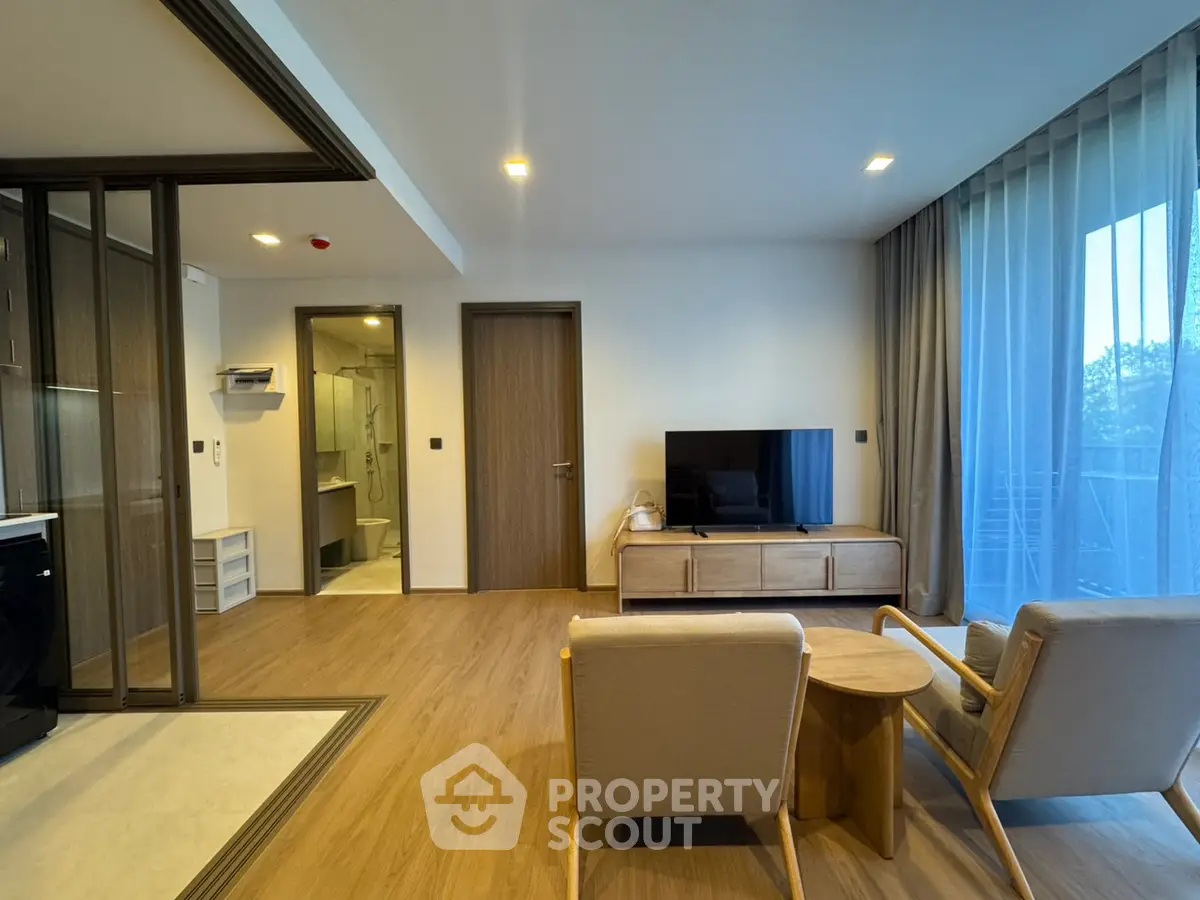 Modern living room with wooden flooring and stylish furniture, featuring a TV and large windows.