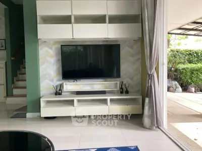 Modern living room with large TV and open patio view, featuring sleek furniture and stylish decor.