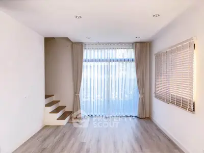 Spacious living room with elegant curtains and wooden flooring, featuring a modern staircase.