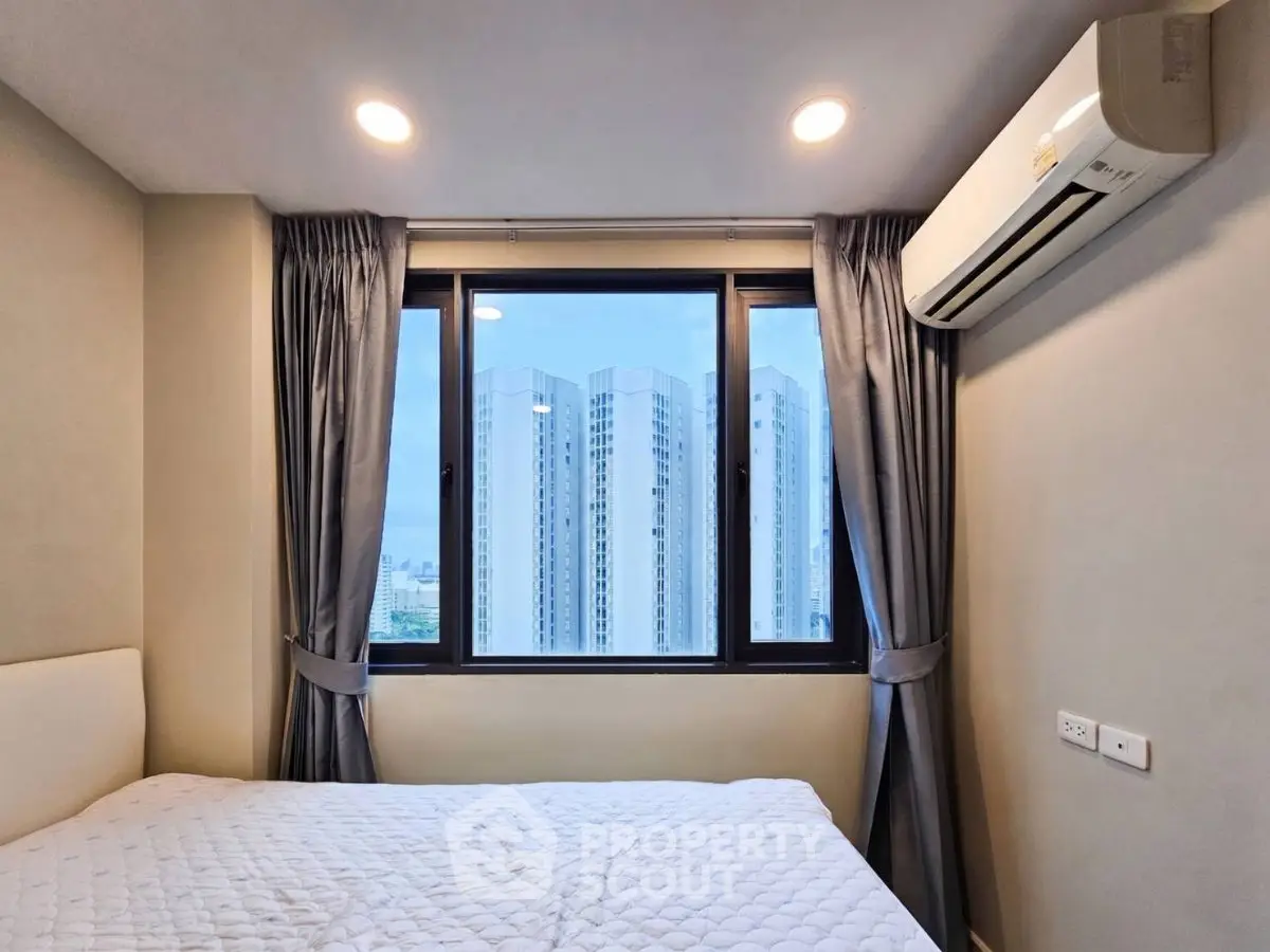 Modern bedroom with city view, featuring large window and air conditioning unit.