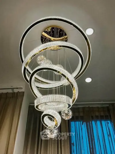 Elegant spiral chandelier in modern living room with high ceiling and large windows.