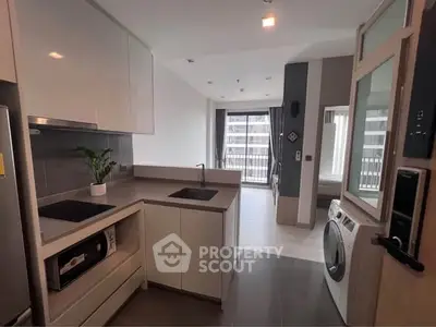 Modern kitchen with sleek appliances and open layout leading to a bright living area with balcony view.