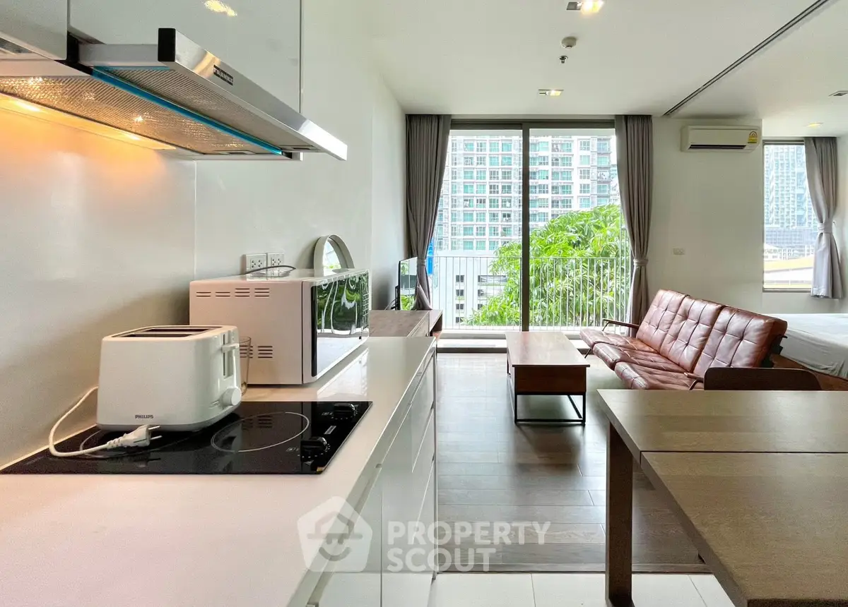 Modern open-plan living room with kitchen, featuring sleek appliances and a spacious balcony view.