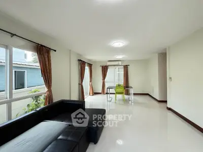 Spacious living room with modern black leather sofa and large windows for natural light.