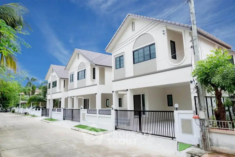 Modern two-story houses with gated driveways and lush greenery in a serene neighborhood.