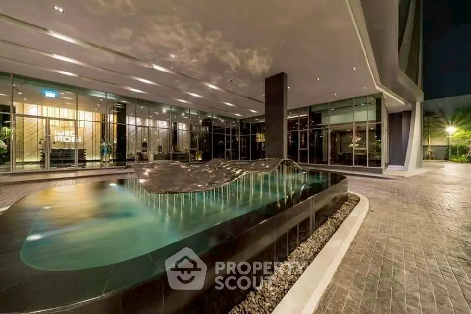 Luxurious modern building entrance with elegant water feature and glass facade at night.