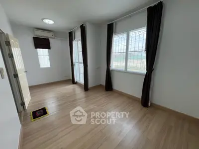 Spacious empty room with wooden flooring and large windows, perfect for customization.