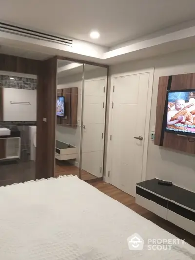 Modern bedroom with mirrored closet and wall-mounted TV in stylish apartment.