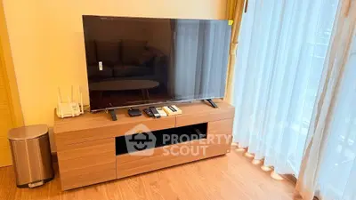 Modern living room with sleek TV setup and natural light through sheer curtains.