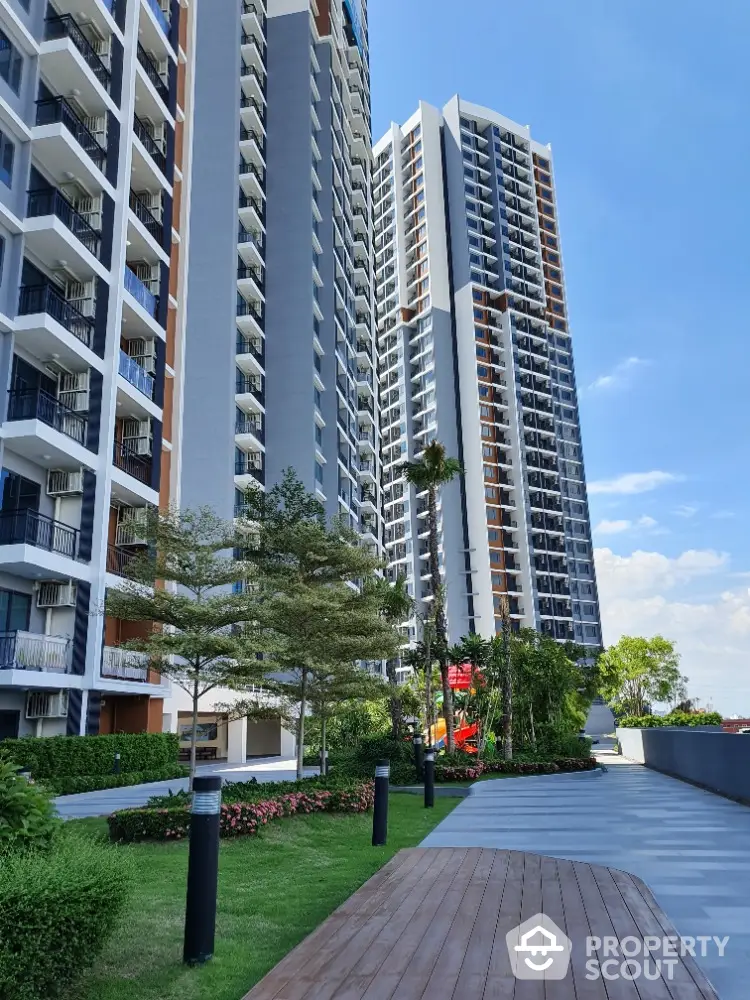 Modern high-rise residential buildings with lush green landscaping and clear blue sky.