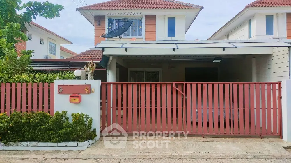 Charming two-story house with red fence and lush greenery in a serene neighborhood.