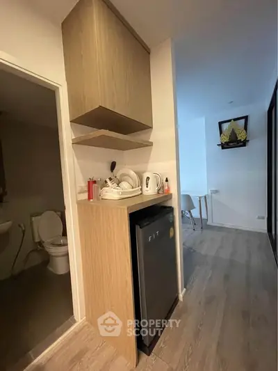 Compact kitchenette with mini fridge and modern wooden cabinetry in cozy apartment.