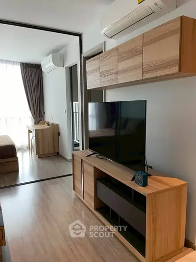Modern living room with wooden furniture and large TV, featuring a glimpse of the bedroom.