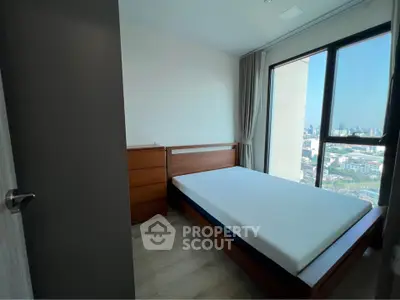 Modern bedroom with large window offering stunning city view, featuring wooden bed and dresser.
