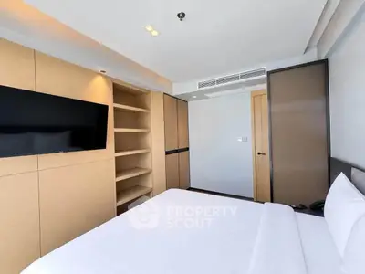 Modern bedroom with built-in storage and flat-screen TV, featuring sleek design and ample natural light.