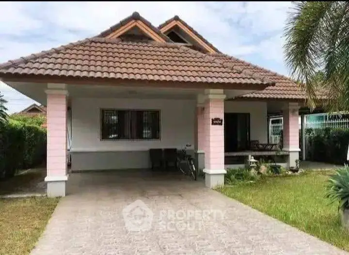 Charming single-story house with tiled roof and spacious driveway, surrounded by lush greenery.