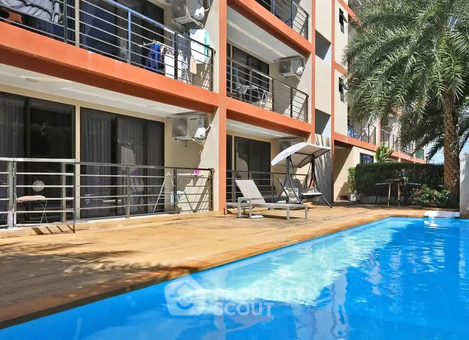 Modern apartment complex with poolside relaxation area and palm trees.