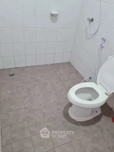 Simple bathroom with tiled floor and walls, featuring a toilet and shower area.