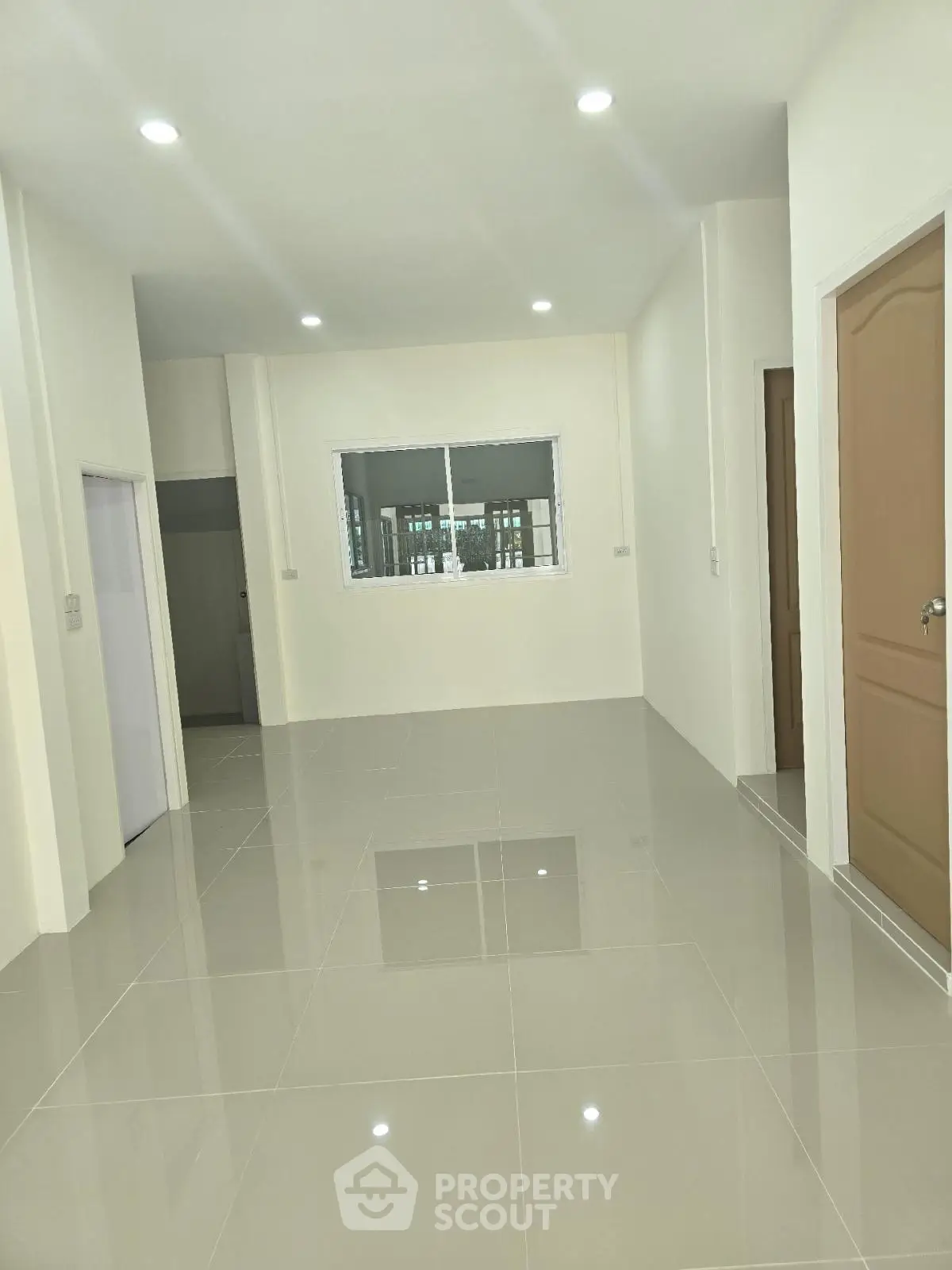 Spacious modern living room with glossy tiled flooring and neutral walls, featuring recessed lighting and a window view.