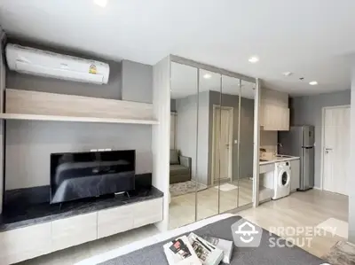 Modern apartment interior with mirrored wardrobe, TV, and compact kitchen area.