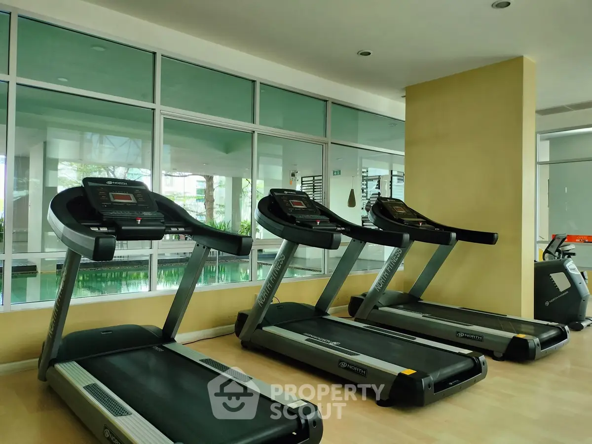 Modern gym with treadmills and large windows overlooking a pool area, perfect for fitness enthusiasts.