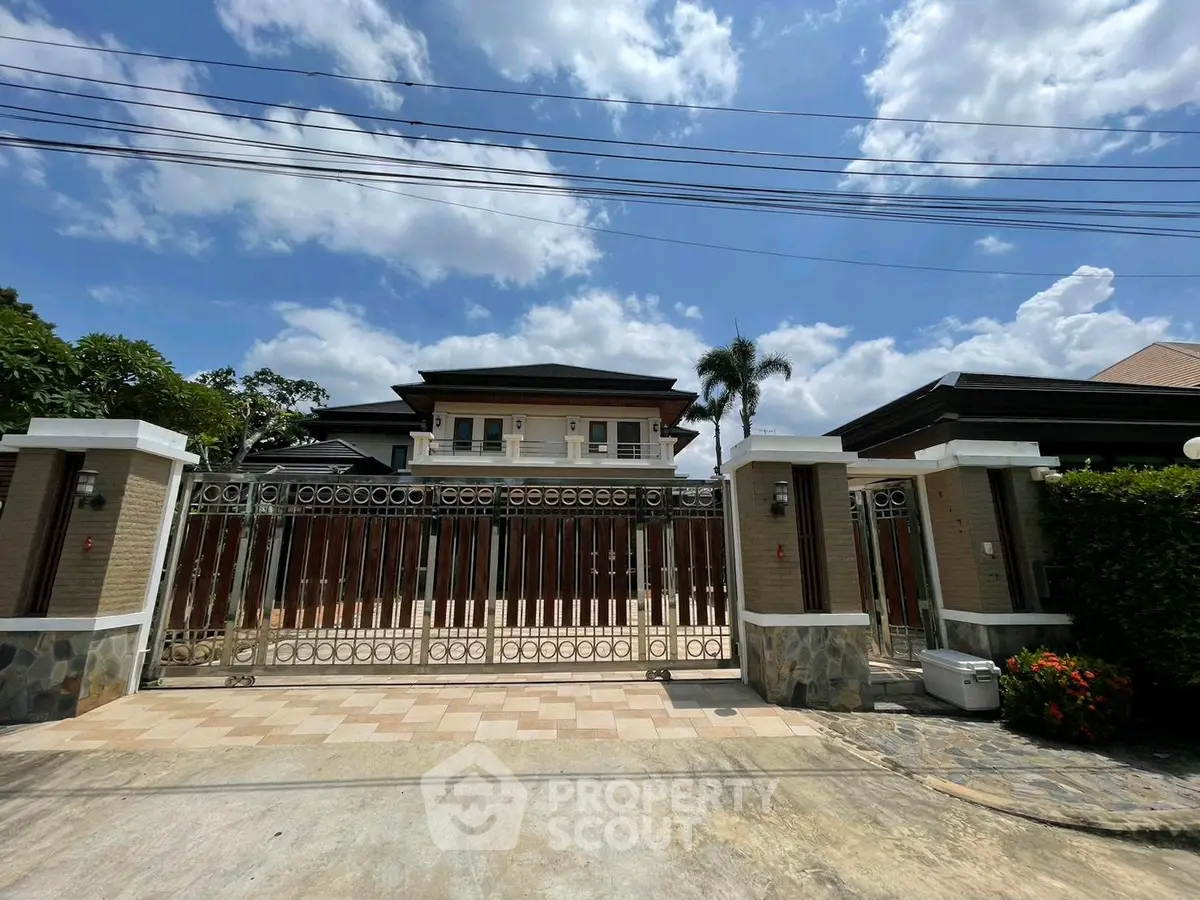 Stunning luxury home with gated entrance and lush landscaping under a bright blue sky.