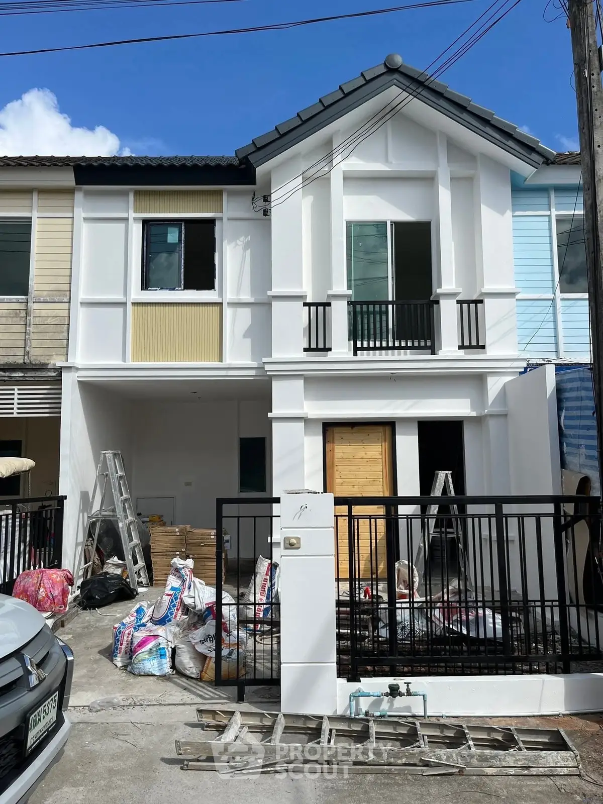 Modern townhouse under renovation with fresh white facade and black railing.