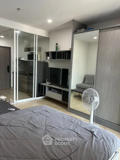Modern bedroom with mirrored wardrobe and compact kitchen area in a stylish apartment.