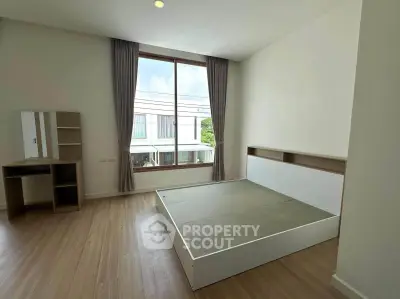 Spacious bedroom with large window and modern furnishings in a bright, airy apartment.