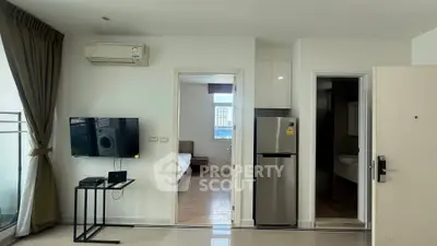 Modern apartment interior with open layout, featuring living area and kitchen with stainless steel fridge.