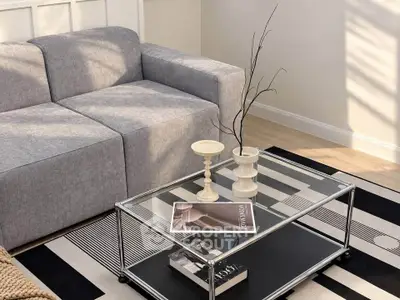Stylish modern living room with sleek gray sofa and chic glass coffee table on striped rug.
