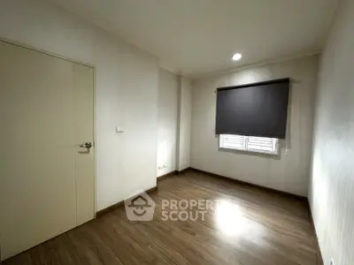 Spacious empty room with wooden flooring and window shade, perfect for customization.