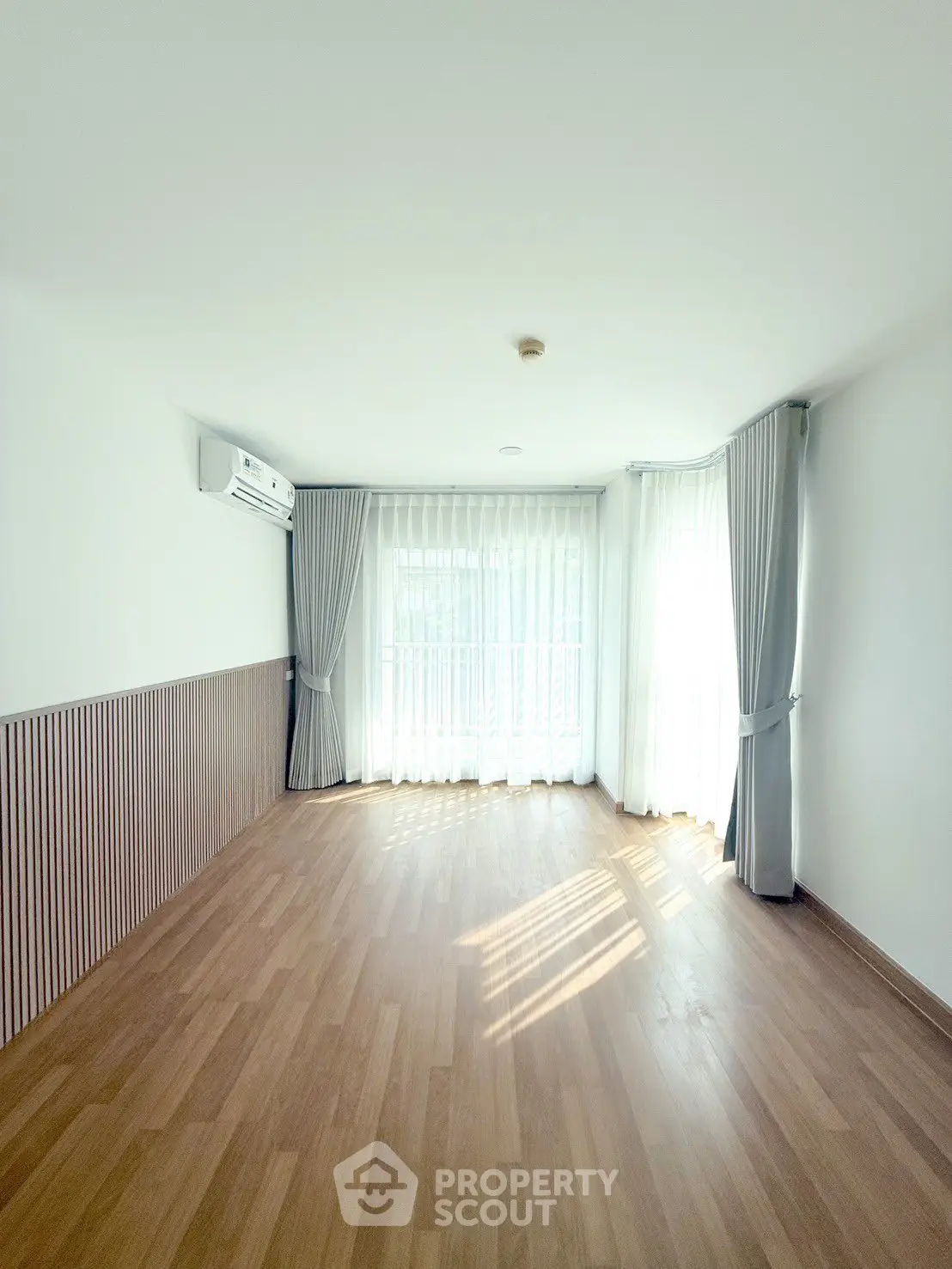 Spacious sunlit room with elegant wooden flooring and large windows in modern apartment.