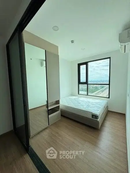 Modern bedroom with large window and wooden flooring, featuring a minimalist design and ample natural light.
