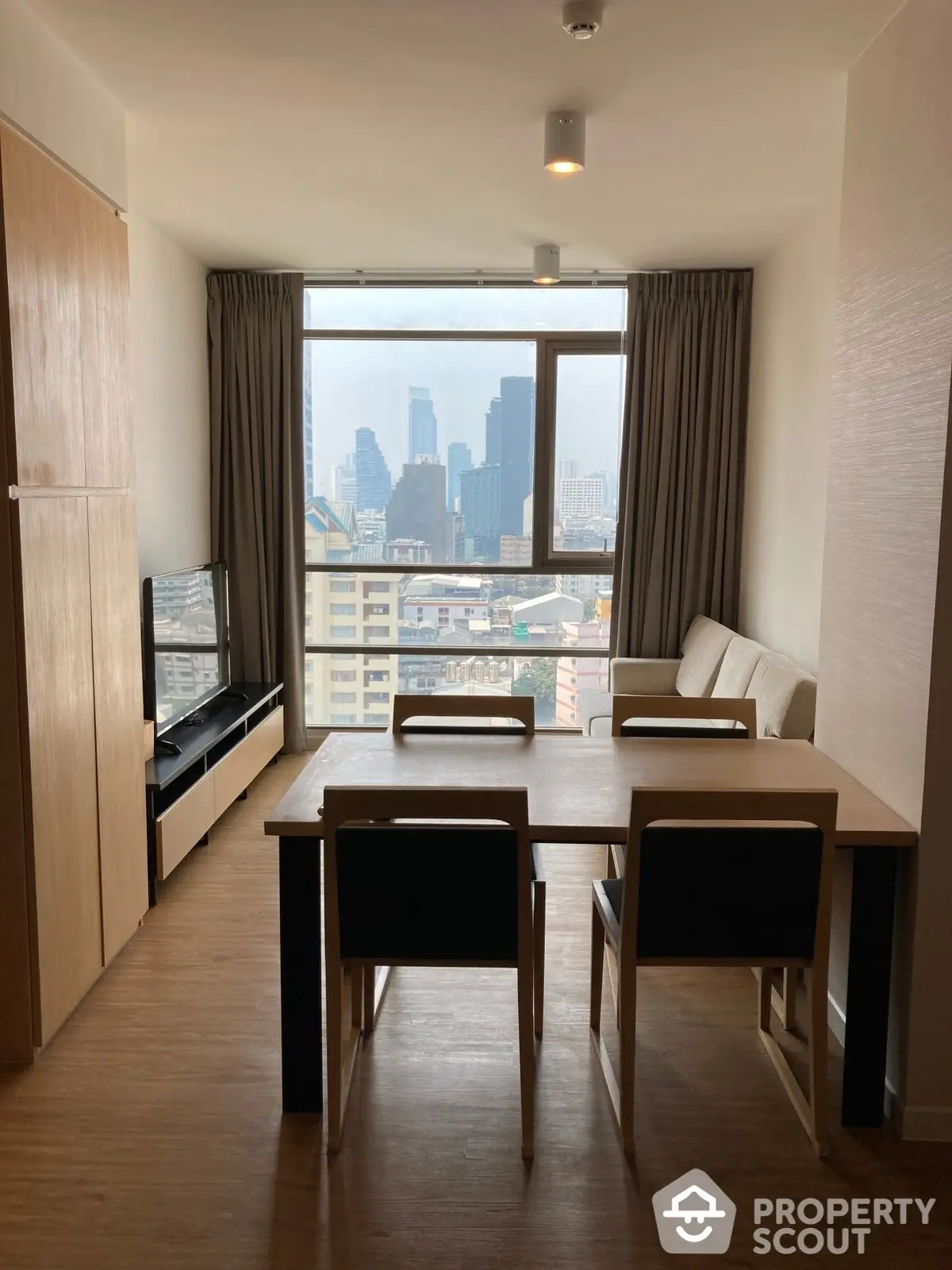 Modern dining area with a stunning cityscape view through a large window, complemented by sleek furniture and warm wooden flooring.