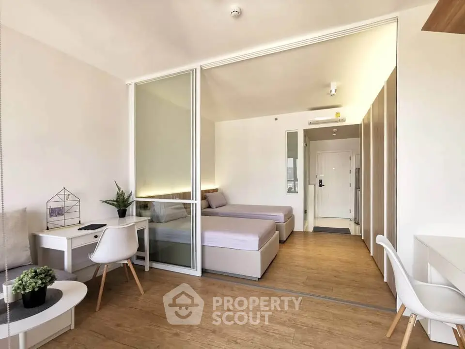 Modern studio apartment with stylish decor and wooden flooring, featuring a cozy living area and twin beds.