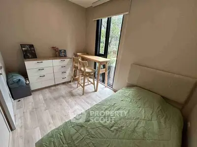 Cozy bedroom with natural light, featuring a single bed, dresser, and small desk by the window.
