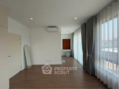 Spacious modern living room with wooden flooring and large windows for natural light.