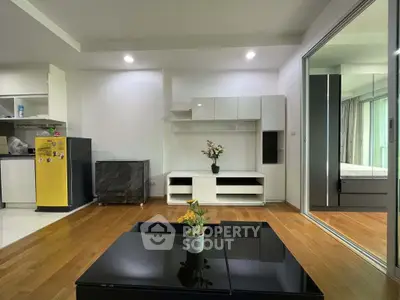 Modern living room with sleek furniture and wooden flooring, adjacent to a compact kitchen area.