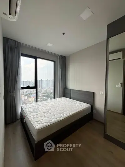 Modern bedroom with large window offering stunning city views in a high-rise apartment.