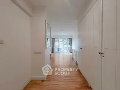 Spacious hallway leading to a bright living area with large windows and wooden flooring.