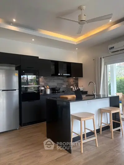 Modern kitchen with sleek black cabinets, island, and stainless steel appliances.