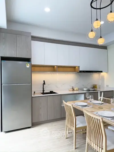 Modern kitchen with sleek cabinetry, stainless steel fridge, and elegant dining area with stylish lighting.