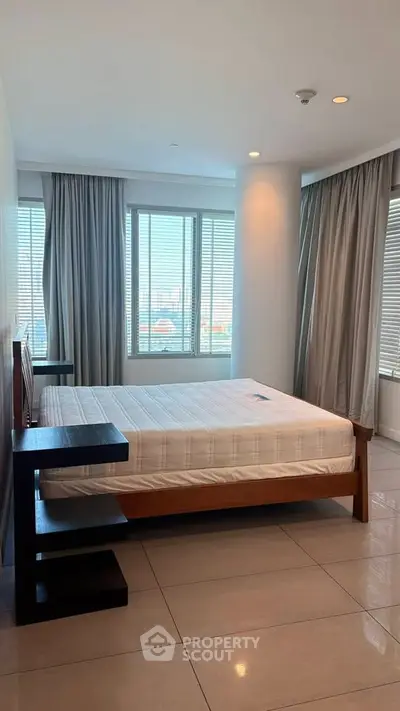 Spacious bedroom with large windows and modern furnishings in a high-rise apartment.